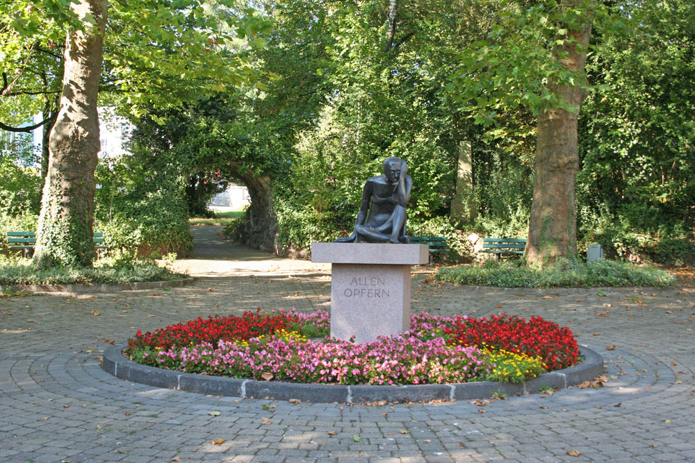 Das Mahnmal trägt den Titel "Allen Opfern" und steht an fast der gleichen Stelle, an der sich in den Jahren zwischen 1925 und 1935 die Skulptur des jüdischen Bildhauers Benno Elkan befand. Dessen Werk wurde 1935 -- in der Zeit des Nationalsozialismus - von Unbekannten entfernt und ist seither verloren.