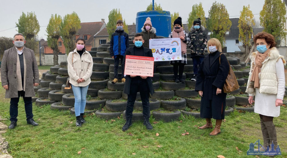 V.l.n.r.: Kamuran Baspinar, Halenur Durgun, Ender Baspinar (Ditib Selimiye Moschee), Oberbürgermeisterin Christiane Blatt und Schulleiterin Petra Pitillo bei der Scheckübergabe auf dem Schulhof der Grundschule. Kinder der Regenbogenschule überreichten im Gegenzug ihr "Danke"-Plakat (Foto: Stadt Völklingen, S.Feß).