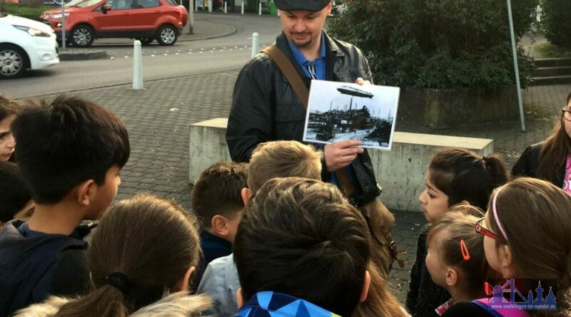 Stadtführer Christian Müller zeigt jungen Teilnehmenden des Stadtrundgangs ein historisches Bild. (Foto: Stadt Völklingen)