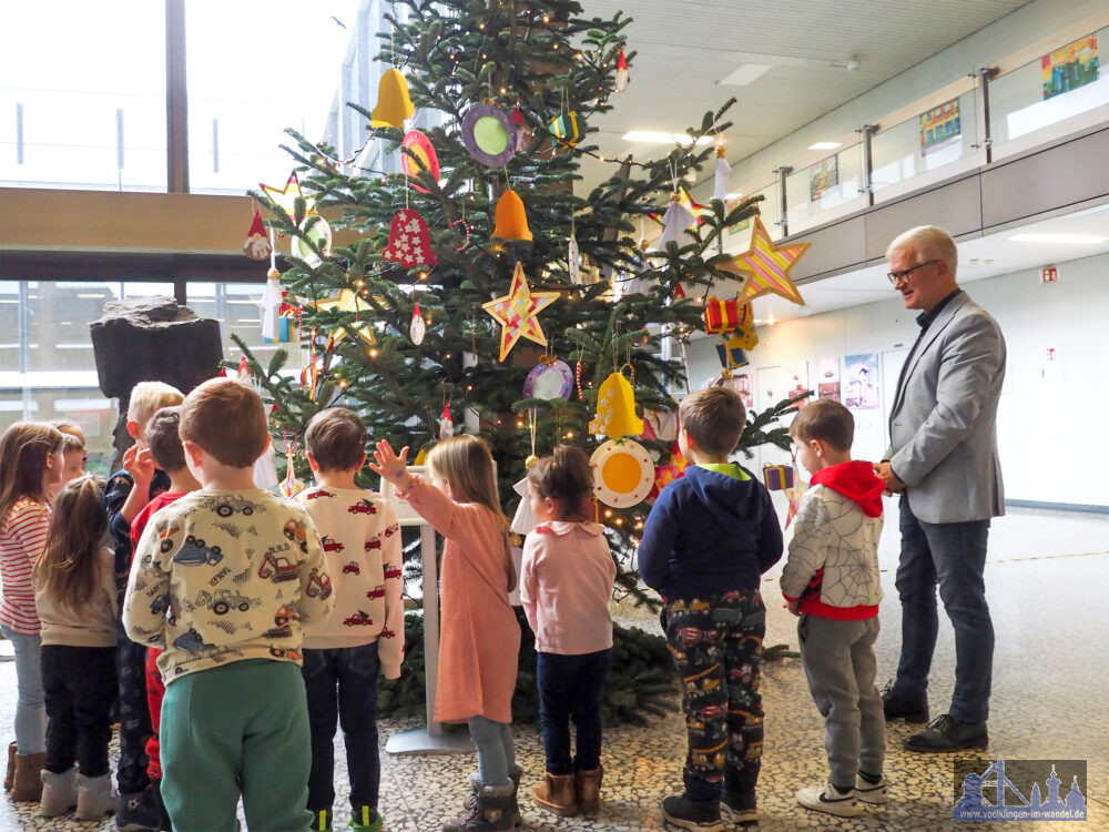 Die Kinder der Kita Lauterbach präsentieren Oberbürgermeister Stephan Tautz (re.) den geschmückten Tannenbaum im Foyer des Neuen Rathauses in Völklingen. Bild: Stadt Völklingen