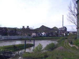Blick 2001 von der Brücke zwischen Völklingen und Wehrden. Im Hintergrund die beiden Schlackenberge "Hermann" und "Dorothea" Links davon zwei "Kühltürme" Rechts davon das inzwischen stillgelegte "Kraftwerk Wehrden". Links: Wehrden mit der neuen Schiffsanlegestelle Im Vordergrund: Die Saar (ehemalige Schleuse) Foto: Andreas Hell 2001